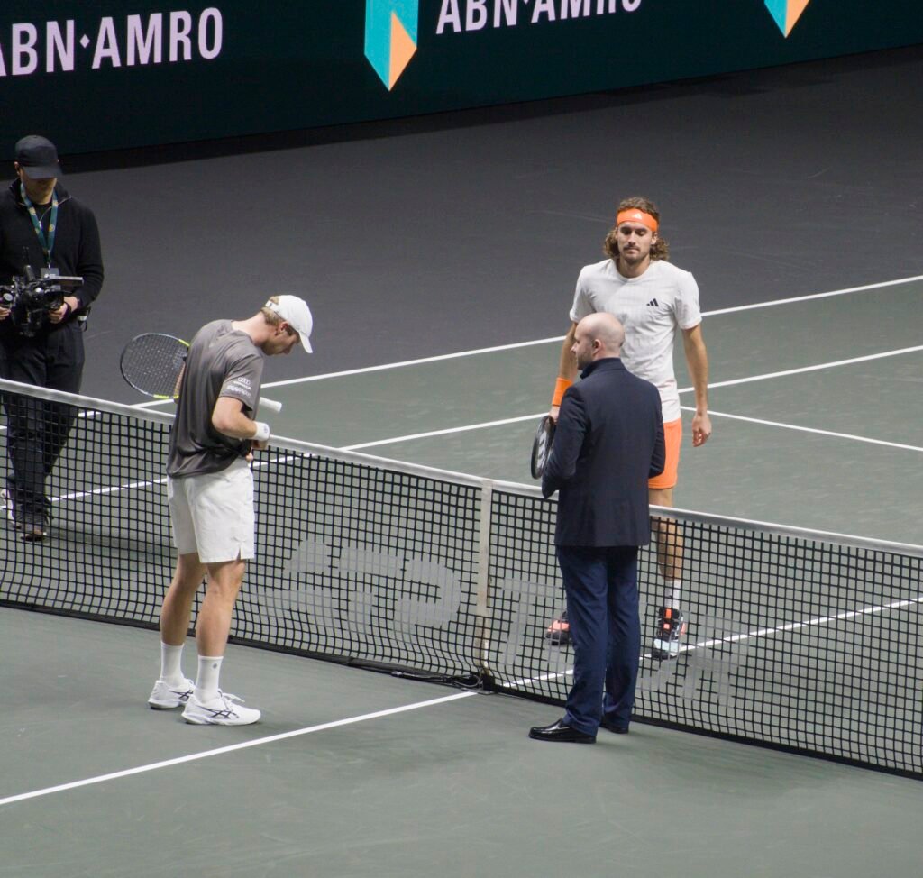 The umpire tosses a coin with Botic van de Zandschulp and Stefanos Tsitsipas before their match at Rotterdam 2026.