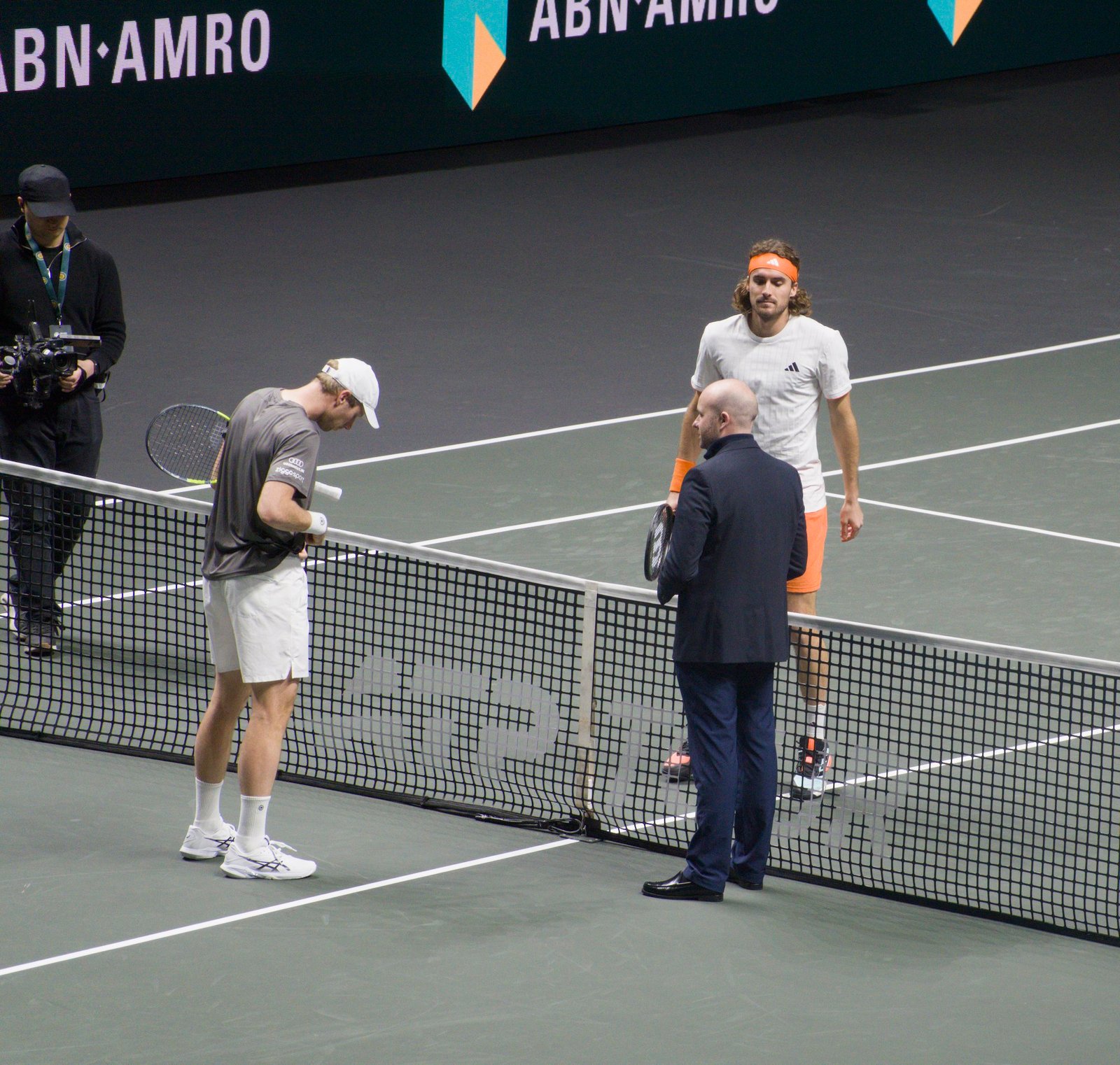The umpire tosses a coin with Botic van de Zandschulp and Stefanos Tsitsipas before their match at Rotterdam 2026.