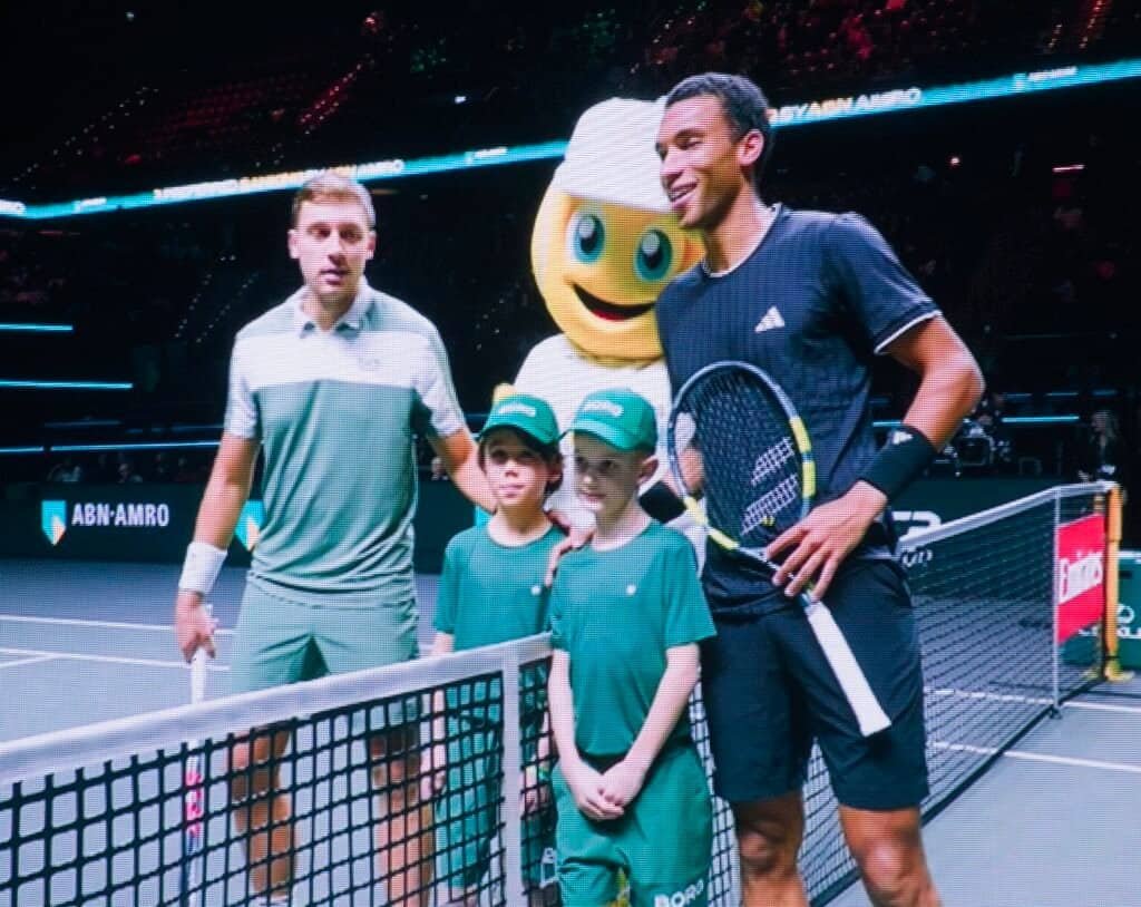 Феликс Оже-Алијасим и Хамад Медјеђевић позирају са маскотом и децом после меча 1/8 финала ABN AMRO Open 2026 Rotterdam ATP 500. ​