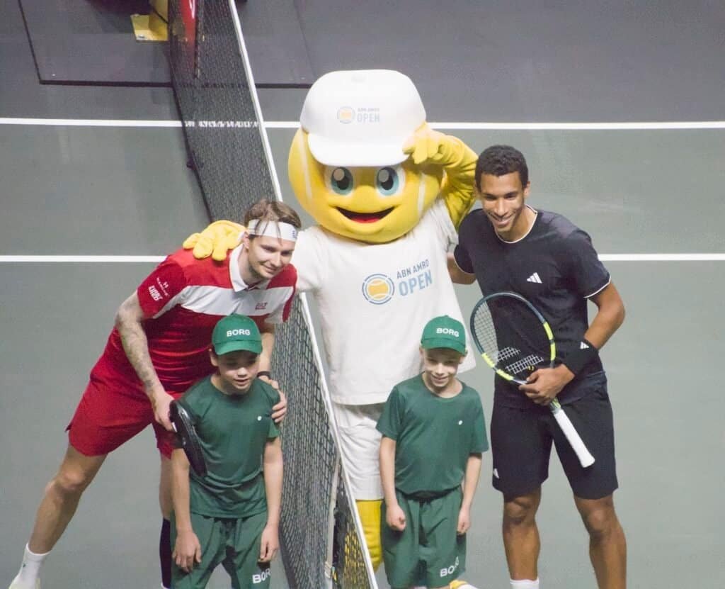 Alexander Bublik and Félix Auger-Aliassime pose at the net with the ABN AMRO Open mascot and two ball kids before their 2026 Rotterdam semi-final.
