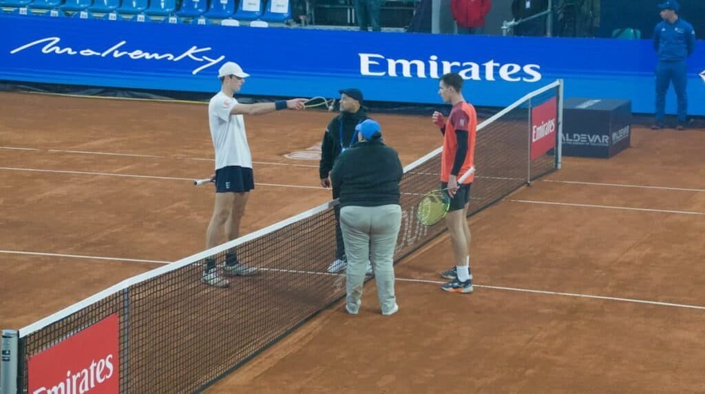 Tennis players Fabian Marozsan and Stefanos Sakellaridis discussing court conditions with the supervisor and umpire during a rain delay.