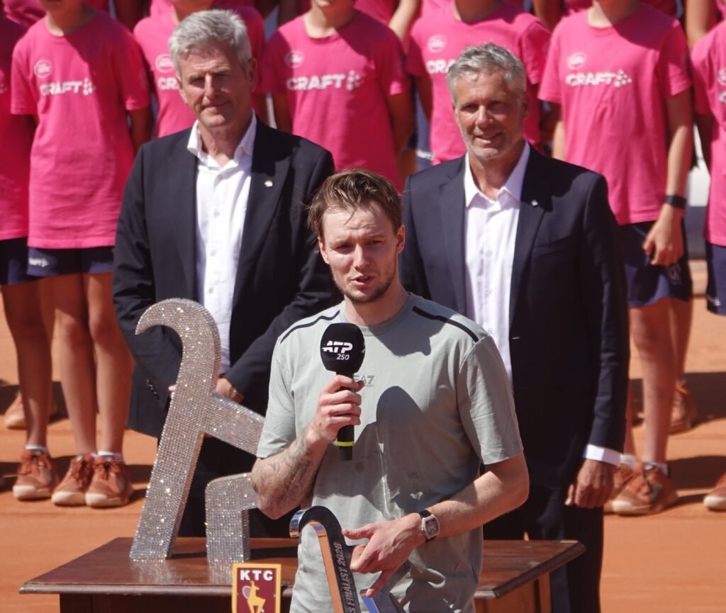 Alexander Bublik giving his runner-up speech next to tournament officials during the 2026 ATP Kitzbuhel trophy ceremony.