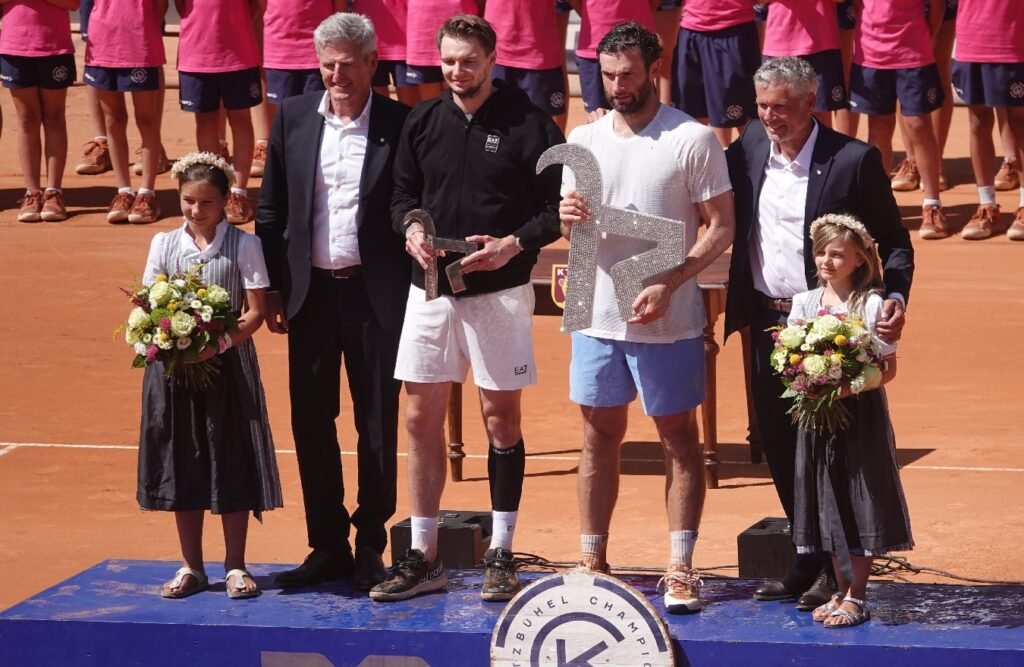 Quentin Halys and Alexander Bublik holding their trophies on the podium with organizers at the 2026 ATP Kitzbuhel tournament.