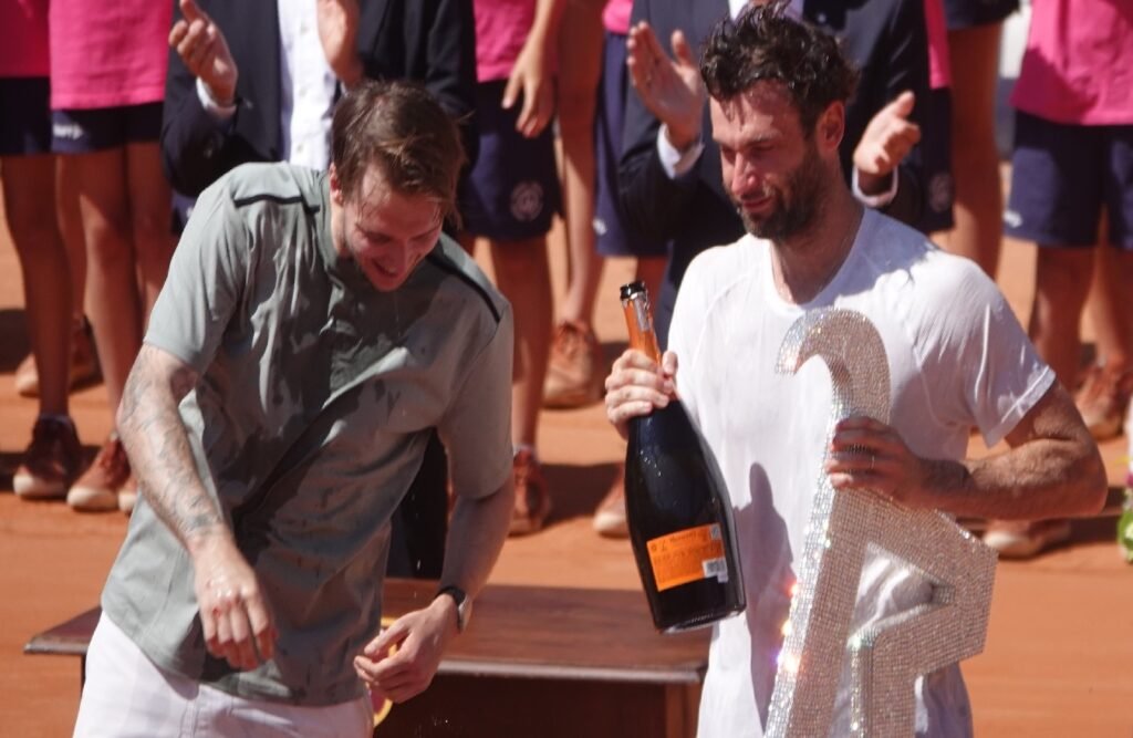 Quentin Halys celebrating with champagne alongside Alexander Bublik during the 2026 ATP Kitzbuhel trophy ceremony.