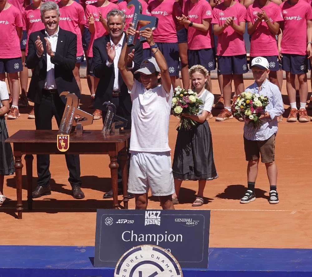 Young tennis player Rafael Pagonis lifting the Kitz Rising champion trophy on the podium alongside tournament officials at the 2026 Generali Open Kitzbuhel.