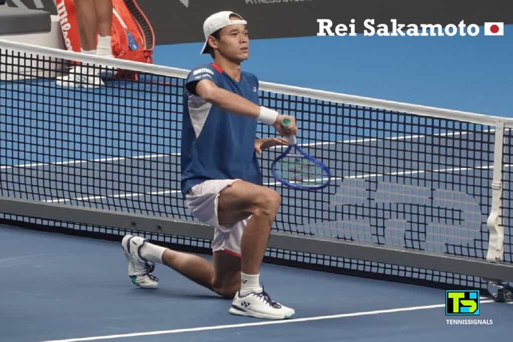 Japanese tennis player Rei Sakamoto kneeling on the court near the net and celebrating his victory by holding his racket like a samurai sword at the ATP Almaty Open.